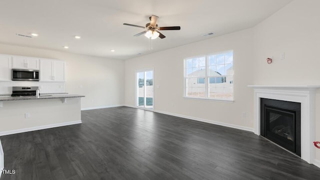 unfurnished living room with dark wood-style flooring, a glass covered fireplace, visible vents, and baseboards