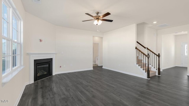 unfurnished living room featuring a wealth of natural light, a glass covered fireplace, dark wood finished floors, and stairs