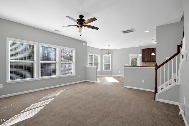 unfurnished living room with stairs, visible vents, carpet flooring, and ceiling fan with notable chandelier