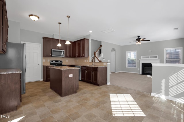 kitchen with arched walkways, stainless steel appliances, open floor plan, a kitchen island, and ceiling fan