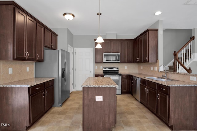 kitchen with dark brown cabinetry, appliances with stainless steel finishes, light stone counters, a center island, and a sink