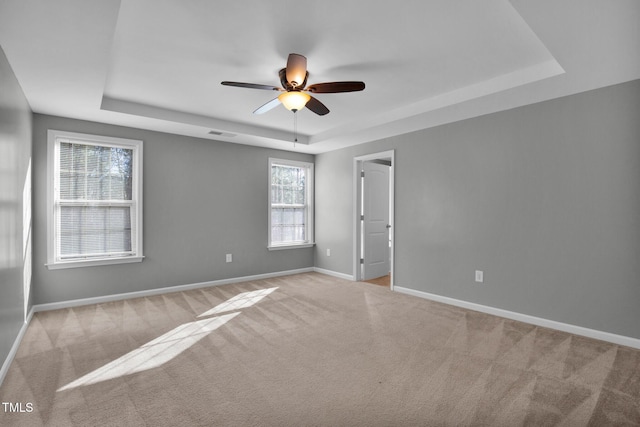 carpeted empty room with baseboards, visible vents, and a tray ceiling