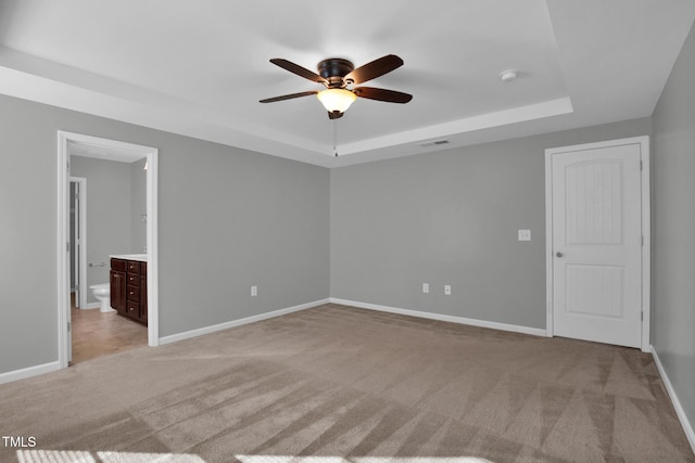 unfurnished bedroom with light carpet, visible vents, a tray ceiling, and baseboards