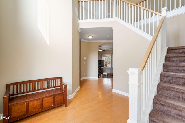 stairs with crown molding, a high ceiling, a ceiling fan, wood finished floors, and baseboards