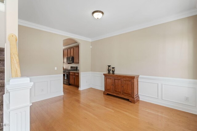 spare room featuring arched walkways, wainscoting, stairway, ornamental molding, and light wood-style floors