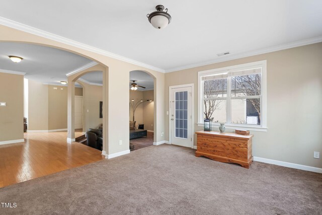 carpeted empty room with visible vents, arched walkways, and ornamental molding