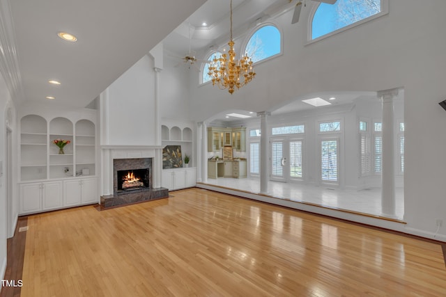 unfurnished living room featuring a high end fireplace, a wealth of natural light, decorative columns, and wood finished floors