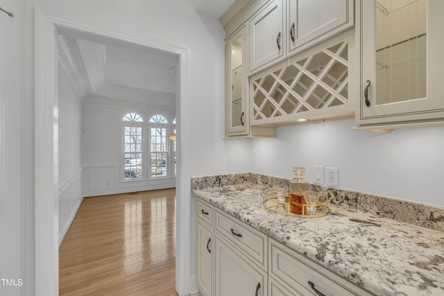 bar featuring a dry bar, a wainscoted wall, light wood-style flooring, crown molding, and a decorative wall