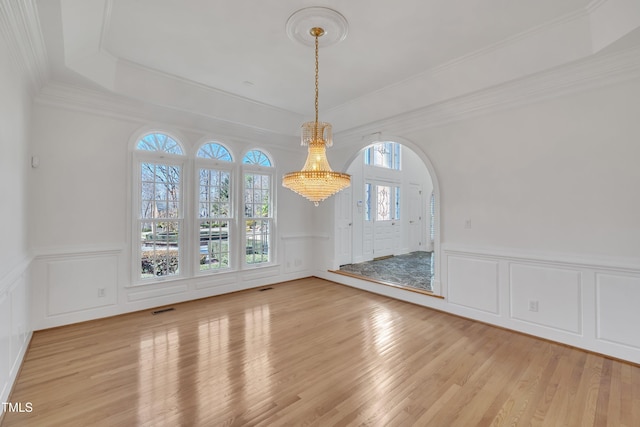 unfurnished dining area featuring arched walkways, a decorative wall, visible vents, light wood finished floors, and crown molding