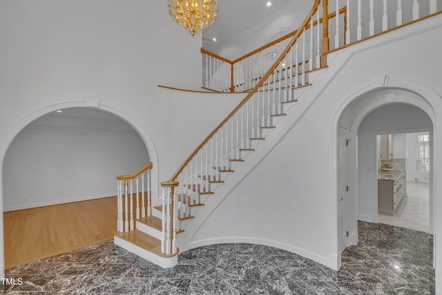 stairway with arched walkways, crown molding, a towering ceiling, baseboards, and an inviting chandelier