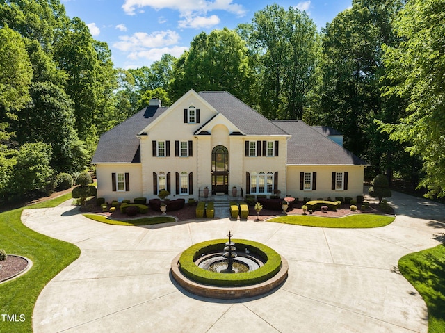 view of front of house featuring roof with shingles, a chimney, curved driveway, and french doors