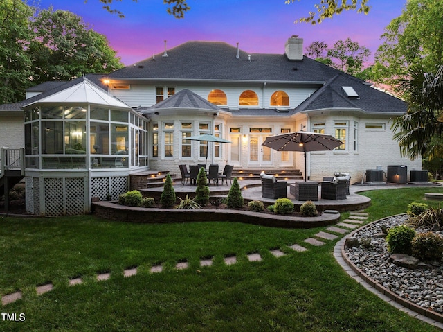 back of property at dusk with a sunroom, a chimney, an outdoor hangout area, and a lawn