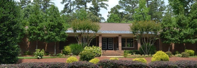 ranch-style house with covered porch, metal roof, brick siding, and a standing seam roof