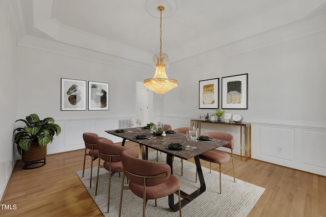 dining area with light wood-style flooring, ornamental molding, a raised ceiling, and a decorative wall