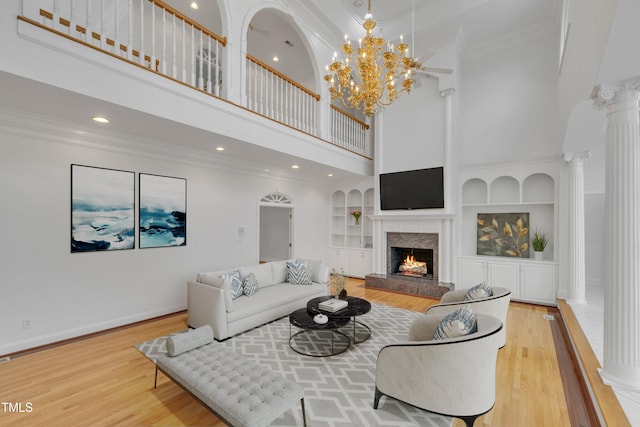 living area with crown molding, ornate columns, a high end fireplace, wood finished floors, and baseboards