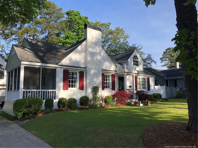 view of front facade featuring a chimney, a sunroom, fence, a balcony, and a front lawn