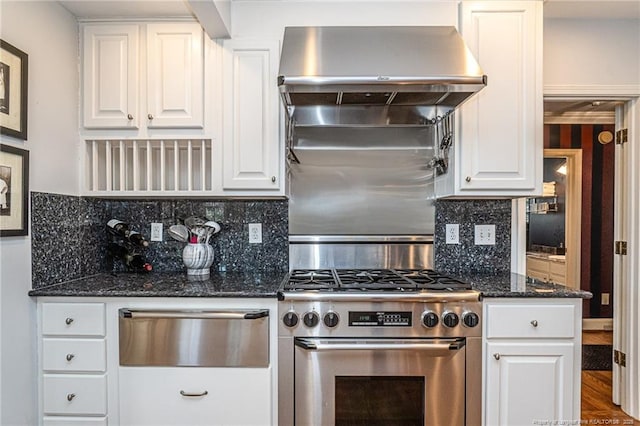 kitchen featuring tasteful backsplash, white cabinets, dark stone countertops, high end stainless steel range, and wall chimney range hood