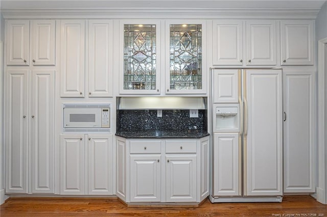 kitchen featuring tasteful backsplash, dark stone counters, glass insert cabinets, built in appliances, and white cabinetry