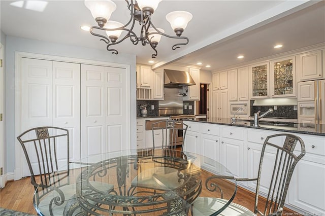 kitchen with premium appliances, backsplash, a notable chandelier, wall chimney range hood, and a sink