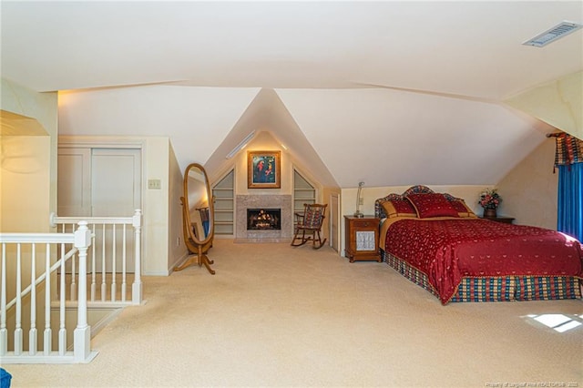 bedroom with vaulted ceiling, carpet floors, a warm lit fireplace, and visible vents