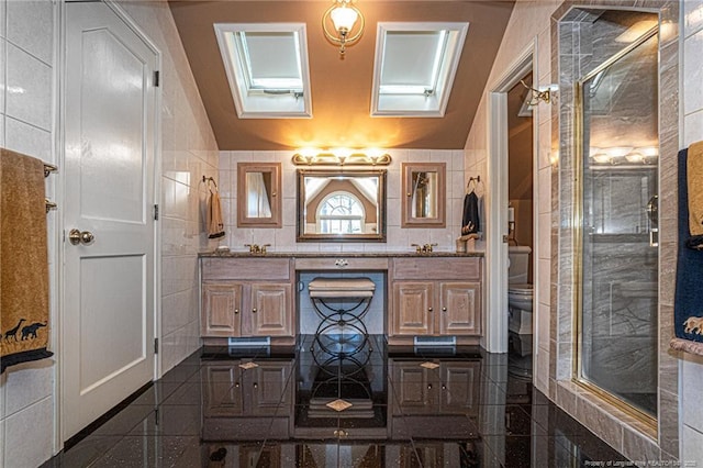 full bath with toilet, granite finish floor, tile walls, double vanity, and a stall shower