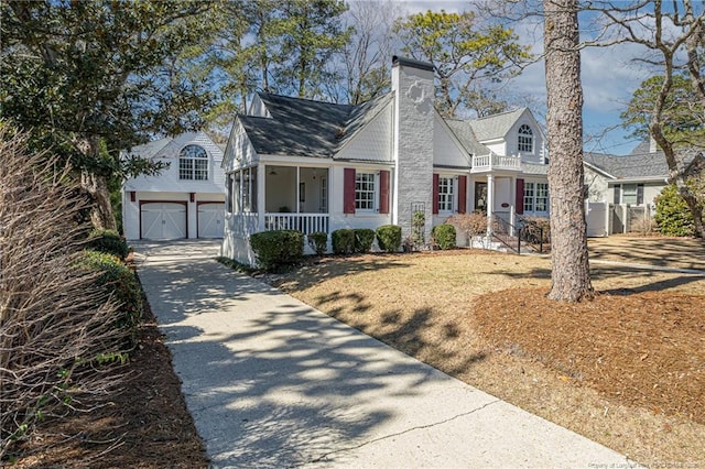 cape cod-style house featuring concrete driveway, a porch, and a chimney