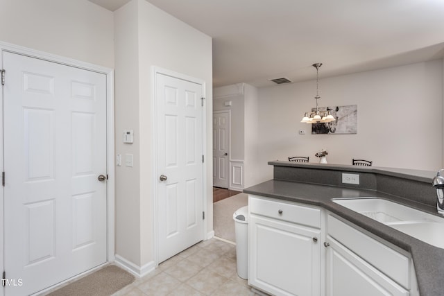 kitchen with an inviting chandelier, a sink, pendant lighting, white cabinetry, and dark countertops