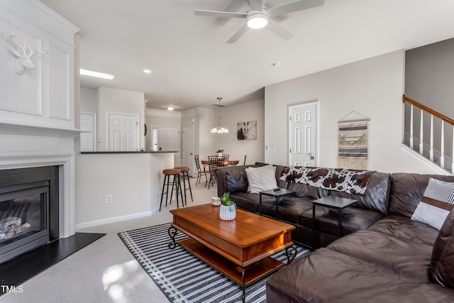 living room with a glass covered fireplace, baseboards, ceiling fan, and stairs