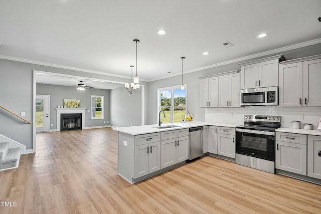 kitchen with appliances with stainless steel finishes, a peninsula, a sink, gray cabinets, and backsplash