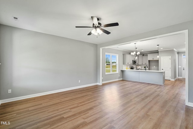 unfurnished living room featuring light wood-type flooring, baseboards, and ceiling fan with notable chandelier