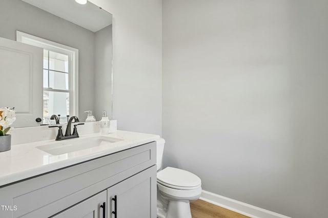 half bathroom featuring wood finished floors, vanity, toilet, and baseboards