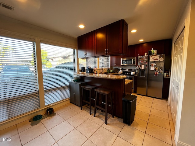 kitchen featuring visible vents, stone countertops, stainless steel appliances, a peninsula, and light tile patterned flooring