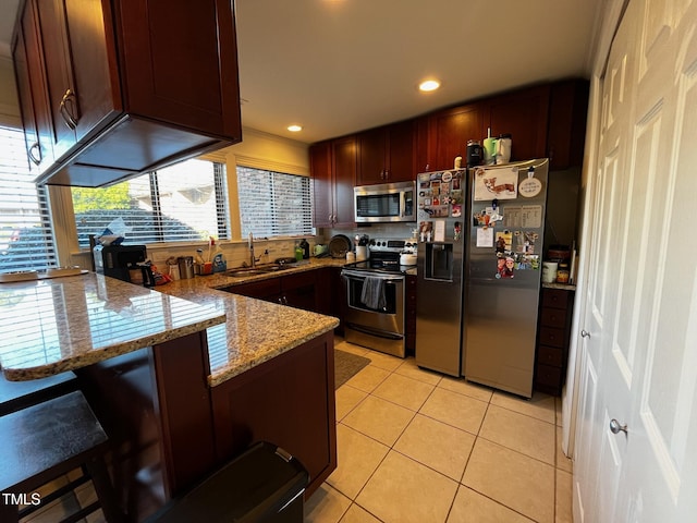 kitchen with light stone countertops, appliances with stainless steel finishes, a peninsula, light tile patterned flooring, and a sink