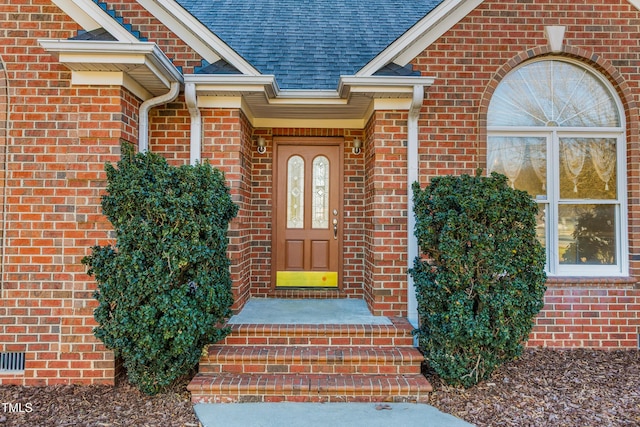 view of exterior entry with roof with shingles and brick siding