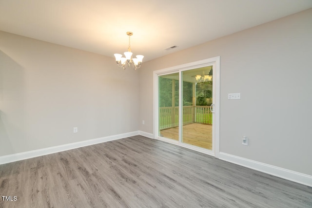 spare room with a notable chandelier, wood finished floors, visible vents, and baseboards