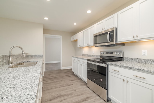 kitchen with light wood finished floors, stainless steel appliances, recessed lighting, white cabinets, and a sink