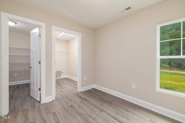 unfurnished bedroom featuring a spacious closet, visible vents, a closet, and wood finished floors