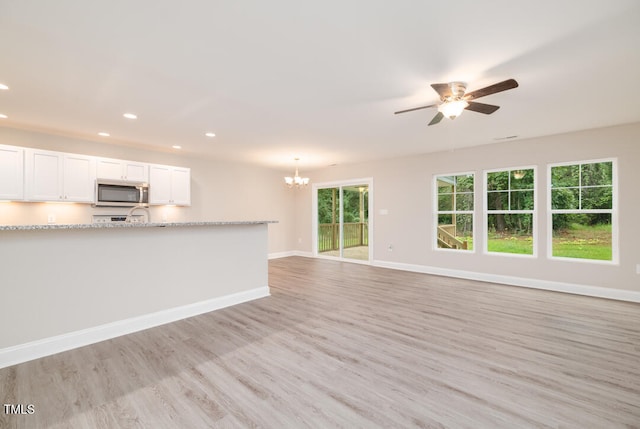 unfurnished living room with light wood-style flooring, ceiling fan with notable chandelier, baseboards, and recessed lighting