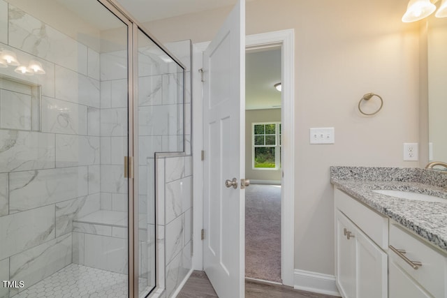 full bath featuring a stall shower, wood finished floors, vanity, and baseboards