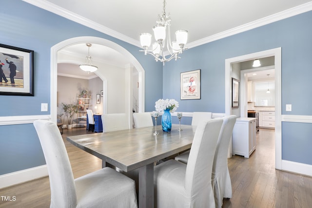 dining area with arched walkways, light wood finished floors, an inviting chandelier, ornamental molding, and baseboards