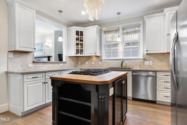 kitchen featuring butcher block countertops, a sink, white cabinets, ornamental molding, and appliances with stainless steel finishes