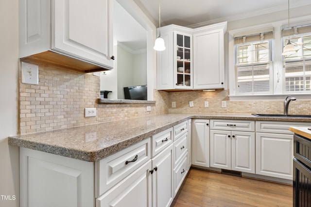 kitchen featuring light wood finished floors, glass insert cabinets, ornamental molding, white cabinetry, and a sink