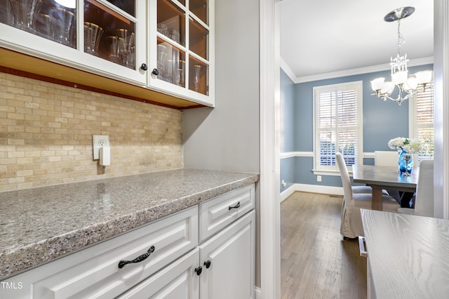 kitchen with white cabinets, glass insert cabinets, ornamental molding, wood finished floors, and backsplash