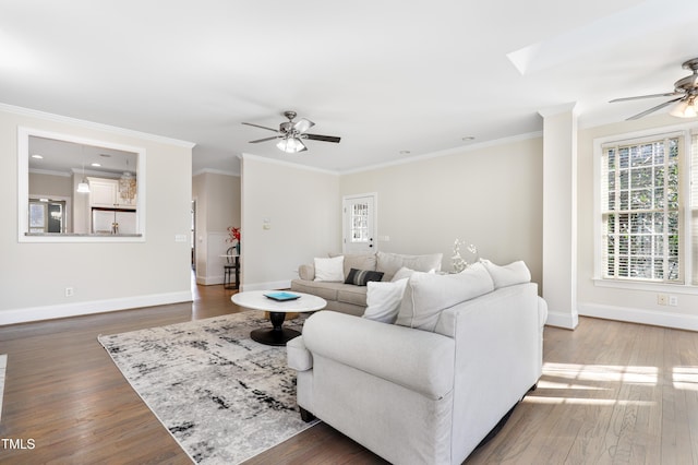 living area with a skylight, wood finished floors, a ceiling fan, baseboards, and ornamental molding