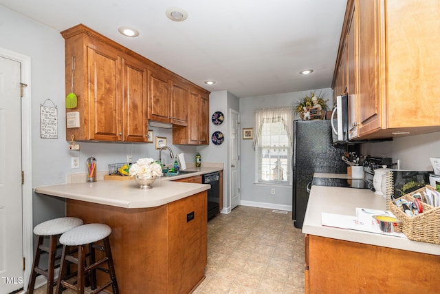 kitchen featuring light countertops, stainless steel microwave, brown cabinetry, a sink, and dishwasher