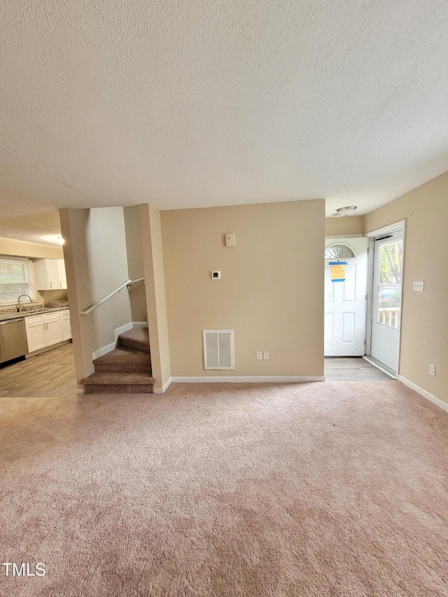 unfurnished living room featuring baseboards, stairway, visible vents, and light colored carpet