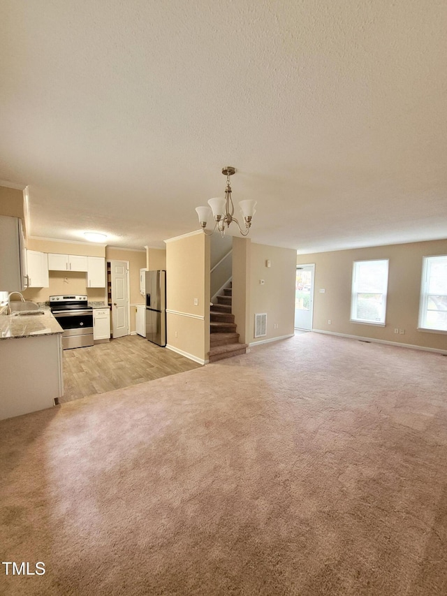 unfurnished living room featuring stairway, light colored carpet, a sink, and visible vents