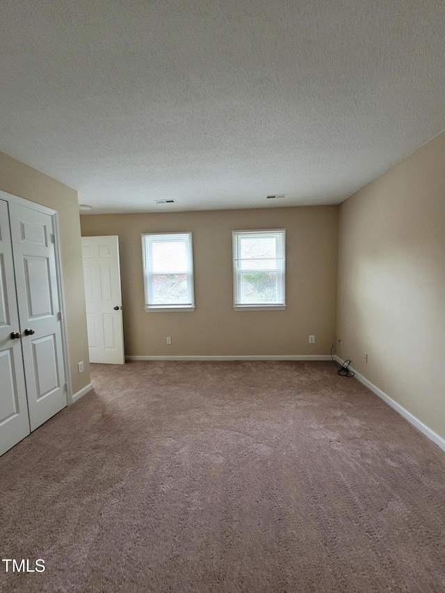 spare room featuring a textured ceiling, carpet, and baseboards