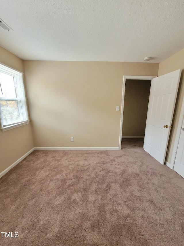 carpeted empty room featuring visible vents, a textured ceiling, and baseboards