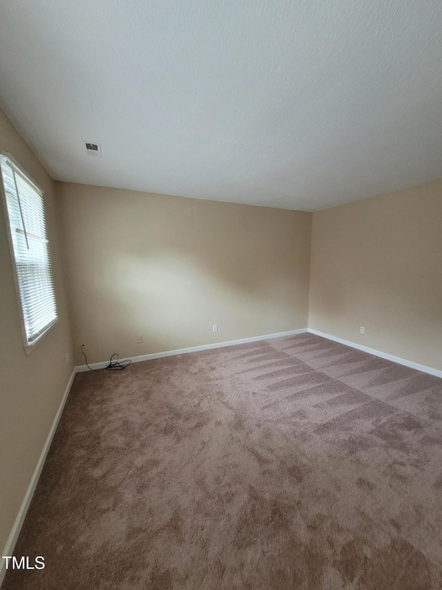 empty room with a textured ceiling, carpet, visible vents, and baseboards